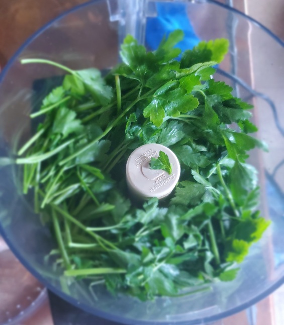 open food processor seen from above containing not-yet mixed parsley stems and leaves