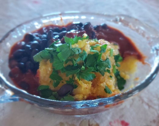 glass dish containing a portion of corn polenta, black beans, red chili sauce and chopped cilantro or parsley