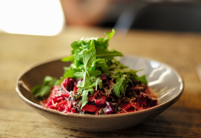 shallow salad bowl containing multicolor beet salad with a pile of arugula on top