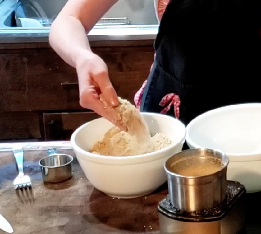 woman's hand mixing powder batter in white porcelain mixing bowls - recipe: sesame ladu
