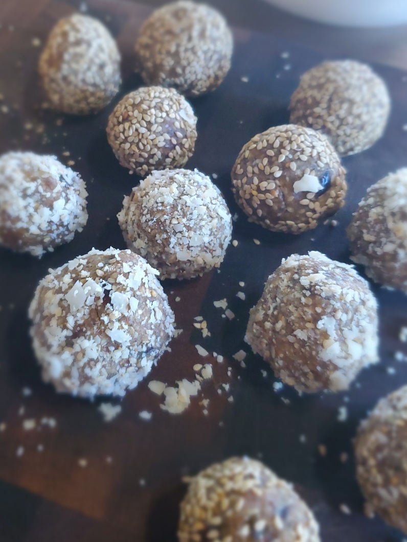 sesame seed sweet dessert balls on wooden board, covered with coconut flakes and sesame seeds: sesame laddu in process